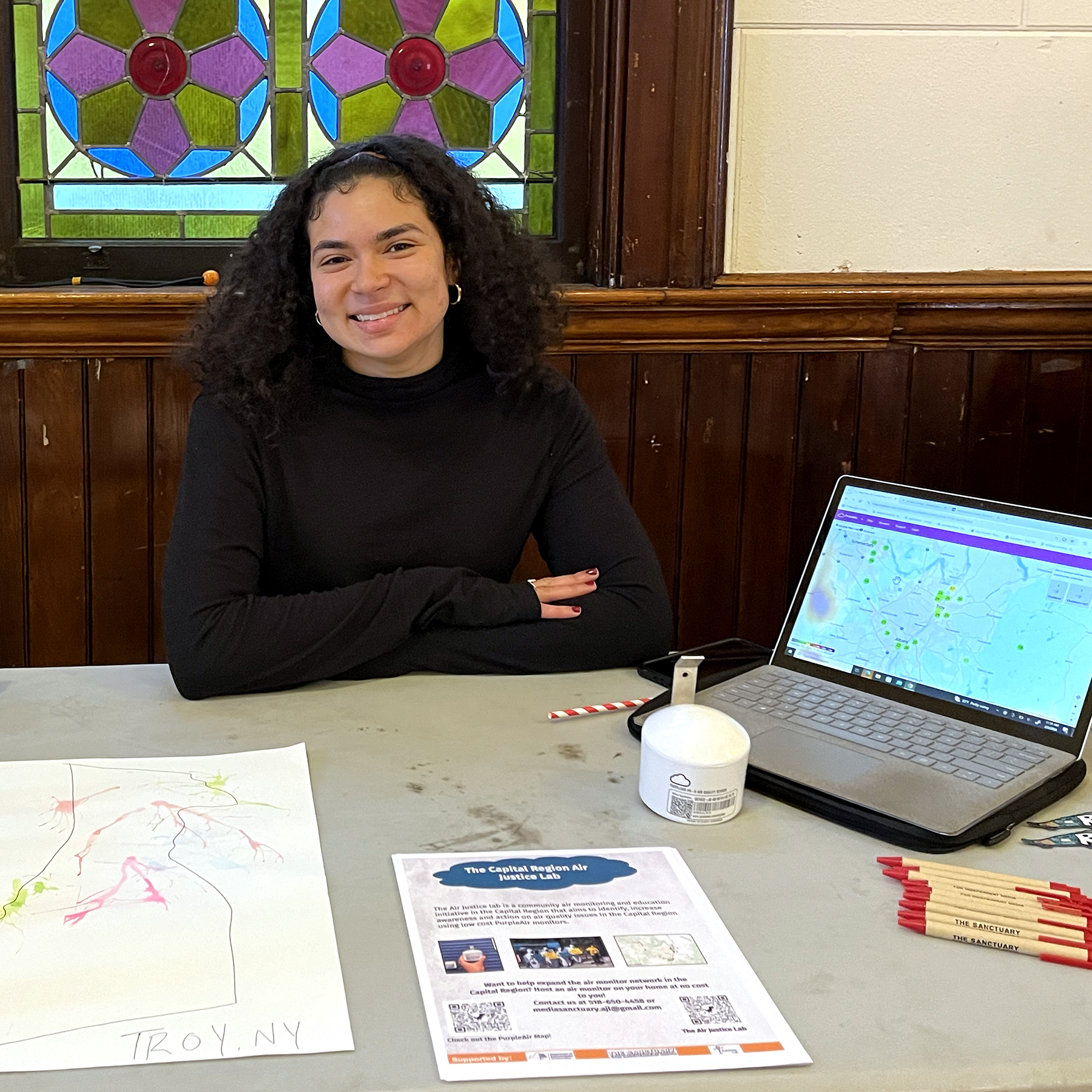 a photo of A’Livija Mullins-Richard sitting at a table to promote the Air Justice Lab using a laptop showing the readings of local air monitors
