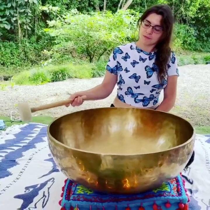 dark haired, light skinned woman stand at 24" wide metal singing bowl with a mallet in her hand.