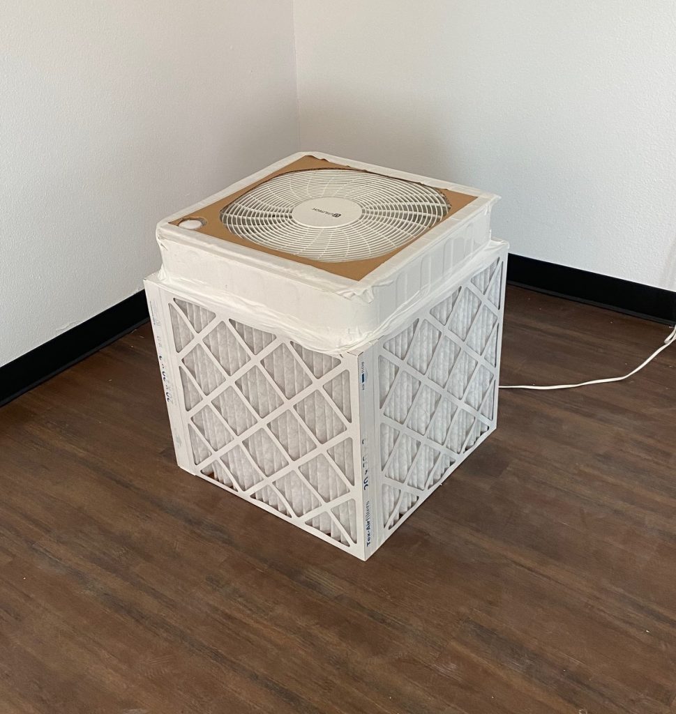 a diy air purifier with with a box fan facing up and air filters on four sides along the base