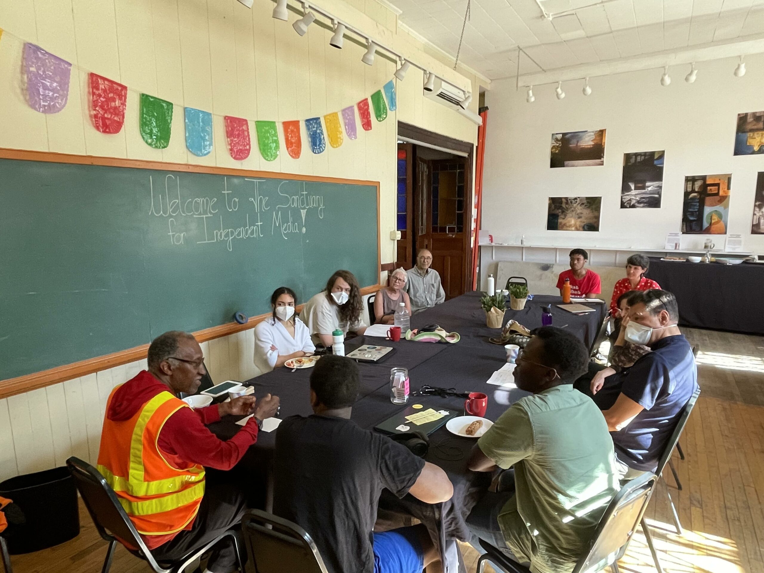 a long table is surrounded by many radio producers of different backgrounds with Willie Terry at the head of the table, leading the discussion